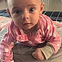 baby, infant, pink_clothing, polka_dots, pillow, blanket, face, wide_eyes, indoor, floor, baby_girl, cute, earrings, hand, expression, baby_bedding, home, child, portrait, tummy_time