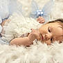 baby, blue_clothing, child, closeup, cute, delicate, face, feathers, hair, indoors, infant, lying_down, newborn, peaceful, portrait, resting, skin, soft_lighting, soft_texture, white_clothing