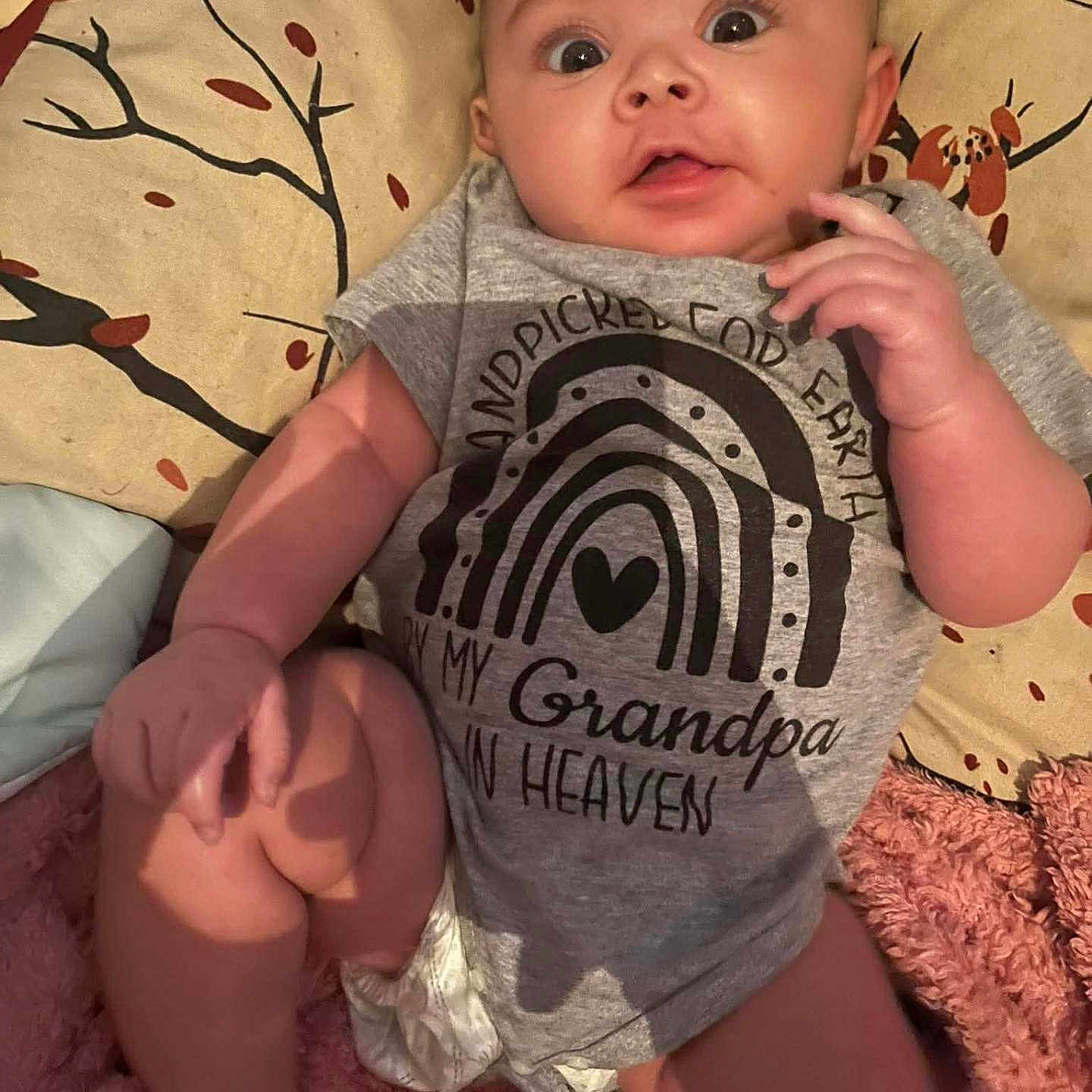 Jayla joined the competition — help win amazing prizes! baby, infant, child, portrait, lying_down, wide_eyed, indoors, bed, bedspread, blanket, onesie, clothing, rainbow, heart, grandpa, smiling, face, hands, legs, cozy