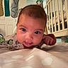 baby, infant, tummy_time, dinosaur_onesie, crib, nursery, soft_toys, playful, curious, indoors, child, face, eyes, expression, blanket, bedroom, person, young_child, cute, home