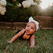 Tala joined the competition — help win amazing prizes! baby, child, grass, flower, garden, outdoor, headband, bow, sunlight, stone_wall, crawling, greenery, nature, cute, young_child, portrait, daylight, happy, face, skin