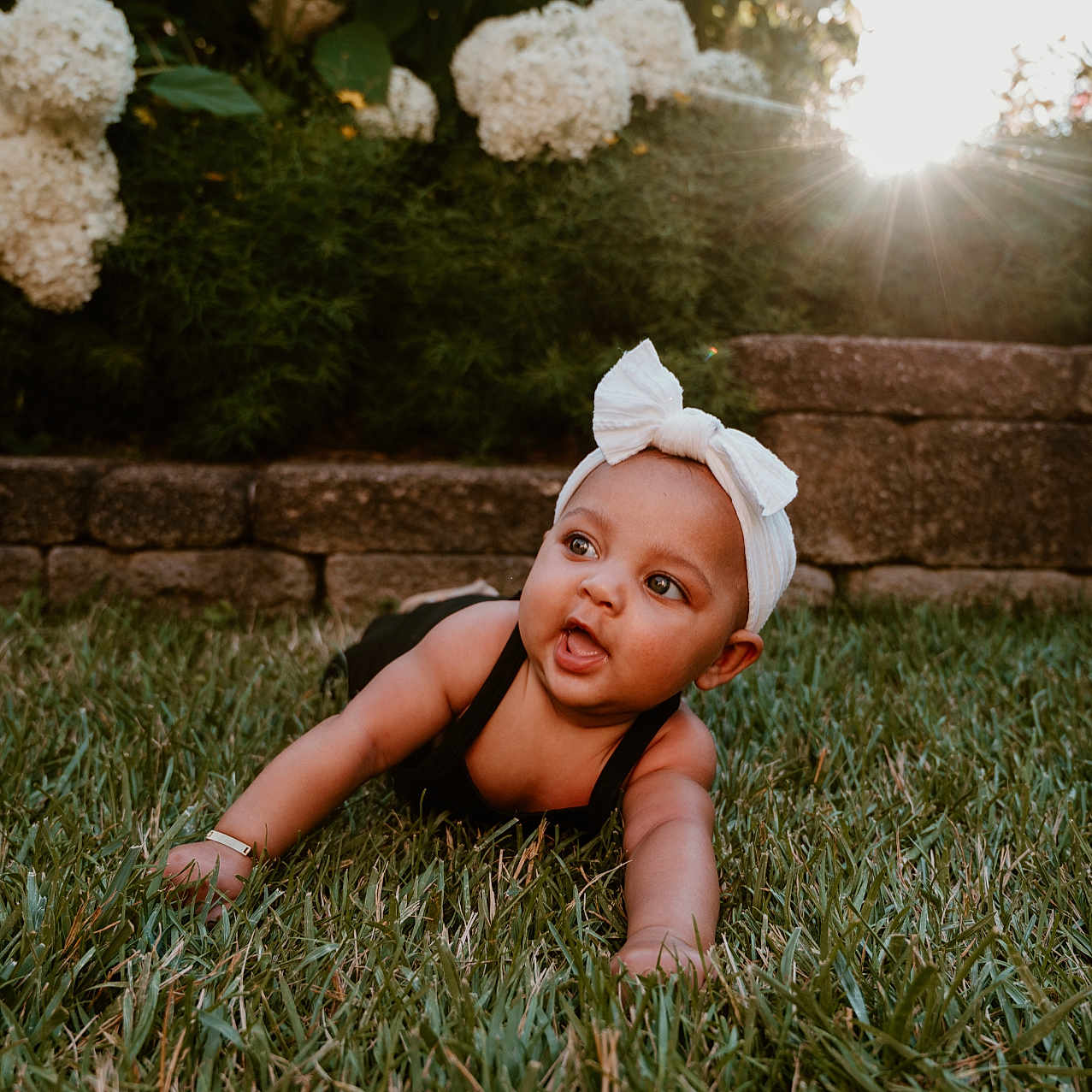 Tala joined the competition — help win amazing prizes! baby, bow, child, crawling, cute, daylight, face, flower, garden, grass, greenery, happy, headband, nature, outdoor, portrait, skin, stone_wall, sunlight, young_child