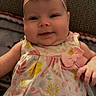 baby, infant, child, smile, headband, bow, dress, floral_pattern, blanket, couch, indoor, person, cute, portrait, happy, skin, baby_clothing, fabric, hand, relaxing