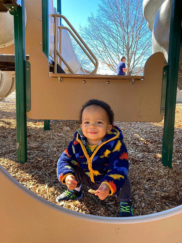 Draco is registered to the contest to win money with this photo: baby_toddler_clothing, child, city, fun, grass, human_settlement, jacket, joy, leisure, nature, outdoor_play_equipment, person, playground, public_space, recreation, shade, sky, sleeve, smile, toddler