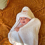 Raphaëlle a rejoint le concours — aidez-le/la à gagner de superbes lots ! baby, towel, hooded_towel, blanket, infant, cute, blue_eyes, wrapped, texture, soft, smiling, happy, child, person, indoor, cozy, white, brown, skin, expression