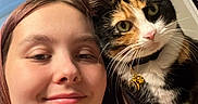 Nymeria is registered to the contest to win money with this photo: woman, person, cat, calico_cat, selfie, portrait, indoors, home, face, eyes, whiskers, fur, collar, bell, long_hair, smiling, close_up, companion_animal, door, warm_lighting