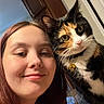 woman, person, cat, calico_cat, selfie, portrait, indoors, home, face, eyes, whiskers, fur, collar, bell, long_hair, smiling, close_up, companion_animal, door, warm_lighting