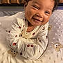 baby, smiling, curly_hair, blanket, teddy_bear, onesie, cherry_print, crib, wooden, cute, infant, happy, face, portrait, bed, soft, child, sleeping_area, cozy, indoors