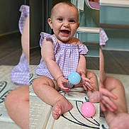 Alannah is registered to the contest to win money with this photo: baby, infant, smiling, laughing, sitting, play_mat, toy_ball, pastel_colors, purple_dress, gingham, cute, toes, legs, eyes, earring, indoor, hardwood_floor, chair, portrait, happy