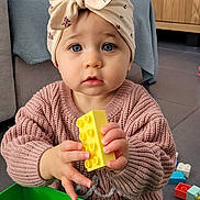 Alice a rejoint le concours — aidez-le/la à gagner de superbes lots ! toddler, child, building_block, toy, headwrap, knit_sweater, indoor, floor, green_container, colorful, blue_eyes, hands, living_room, wooden_cabinet, television, playtime, curious, plastic_toy, floor_tiles, furniture