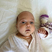 Emma a rejoint le concours — aidez-le/la à gagner de superbes lots ! baby, infant, face, eyes, hand, onesie, clothing, bed, sheet, knitted_toy, purple, white, soft_toy, newborn, cute, child, portrait, lying_down, indoors, skin