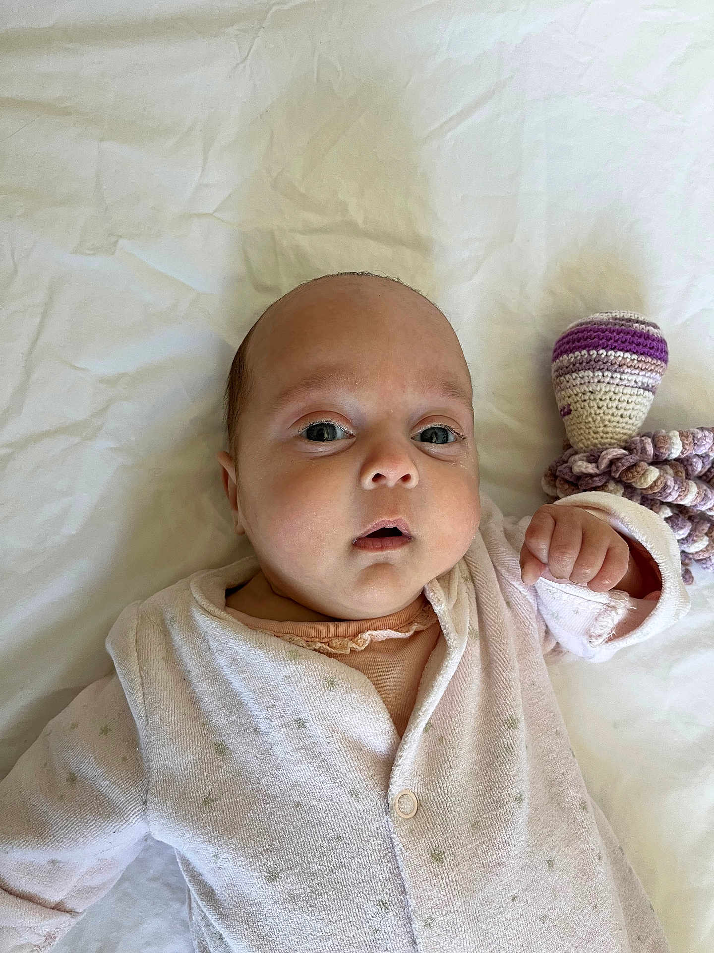Emma a rejoint le concours — aidez-le/la à gagner de superbes lots ! baby, infant, face, eyes, hand, onesie, clothing, bed, sheet, knitted_toy, purple, white, soft_toy, newborn, cute, child, portrait, lying_down, indoors, skin