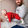 Freddie is registered to the contest to win money with this photo: baby, man, beard, smiling, holding, red_clothing, white_socks, festive_sweater, holiday_decor, gifts, indoor, portrait, happy, family, child, casual, seated, background_decor, cozy, celebration