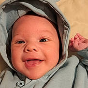 Freddie is registered to the contest to win money with this photo: baby, smiling, hoodie, blue_clothing, infant, face, happy, cute, lying_down, child, apparel, one_person, portrait, headwear, indoors, skin, eyes, mouth, hand, fabric