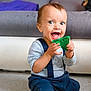 baby, child, toy, green_toy, smiling, happy, indoor, floor, sitting, clothing, striped_shirt, suspenders, pants, face, person, furniture, sofa, cushion, home, play