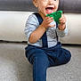 Tiago a rejoint le concours — aidez-le/la à gagner de superbes lots ! toddler, child, smiling, blue_pants, striped_shirt, sitting, toy, green_toy, indoors, floor, barefoot, happy, person, face, eyes, couch, furniture, home, suspenders, play