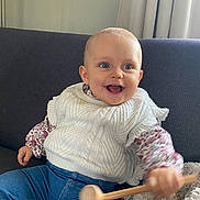Charline participe au concours pour gagner de l'argent avec cette photo : baby, child, smiling, happy, indoor, couch, white_sweater, blue_jeans, wooden_mallet, toy, curtains, floral_shirt, face, person, seated, cozy, cute, home, infant, playful