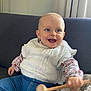 baby, child, smiling, happy, indoor, couch, white_sweater, blue_jeans, wooden_mallet, toy, curtains, floral_shirt, face, person, seated, cozy, cute, home, infant, playful