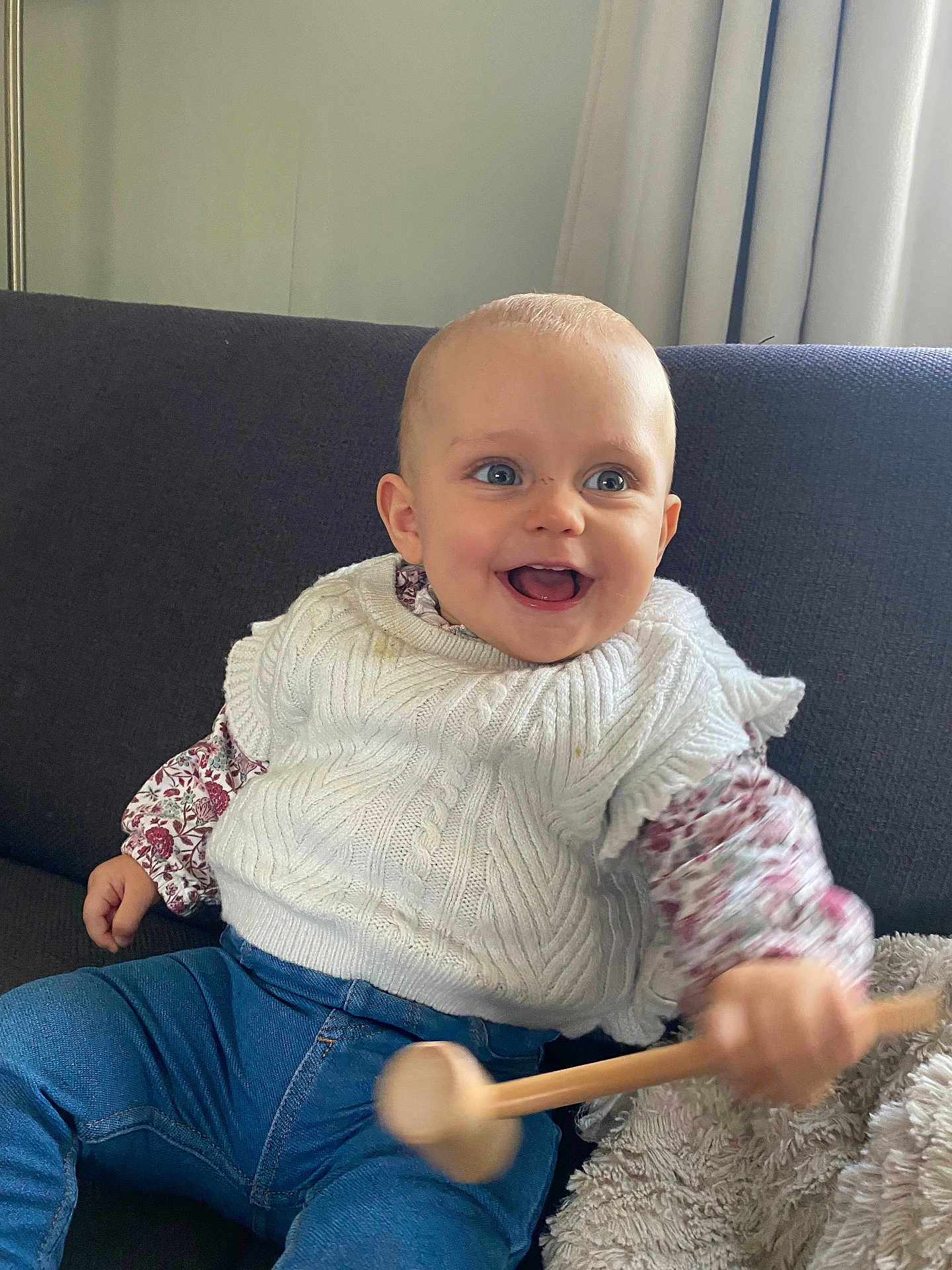 Charline participe au concours pour gagner de l'argent avec cette photo : baby, child, smiling, happy, indoor, couch, white_sweater, blue_jeans, wooden_mallet, toy, curtains, floral_shirt, face, person, seated, cozy, cute, home, infant, playful