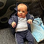 baby, child, infant, hoodie, tracksuit, couch, blanket, pillow, curious, seated, clothing, indoor, portrait, face, hand, expression, fabric, text_on_clothing, blue, white