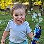 child, toddler, bubble, bubble_gun, toy, outdoors, backyard, grass, trees, smile, tongue_out, happy, portrait, candid, striped_shirt, short_hair, playtime, daylight, greenery, casual_clothing