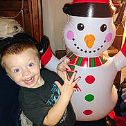 Colton is registered to the contest to win money with this photo: child, toddler, smiling, indoor, inflatable, snowman, holiday, christmas, toy, happy, person, clothing, short_hair, face, cheerful, furniture, bedroom, wood, scarf, hat