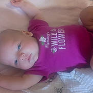 Ora is registered to the contest to win money with this photo: baby, infant, lying_down, pink_clothing, onesie, blanket, blue_eyes, soft_surface, cute, child, newborn, portrait, indoor, person, sleepwear, young_child, baby_girl, text_on_clothing, relaxed, cozy