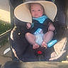 baby, car_seat, hat, sun_hat, diaper, infant, outdoor, child, blue_clothing, seatbelt, sunlight, sidewalk, footwear_absent, cute, small, baby_face, baby_toy, baby_accessory, shade, summer