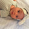 baby, infant, child, portrait, lying_down, headband, bow, onesie, plaid_clothing, blanket, bedding, patterned_background, zigzag_pattern, wide_eyes, face, eyes, indoor, cozy, photography, adorable