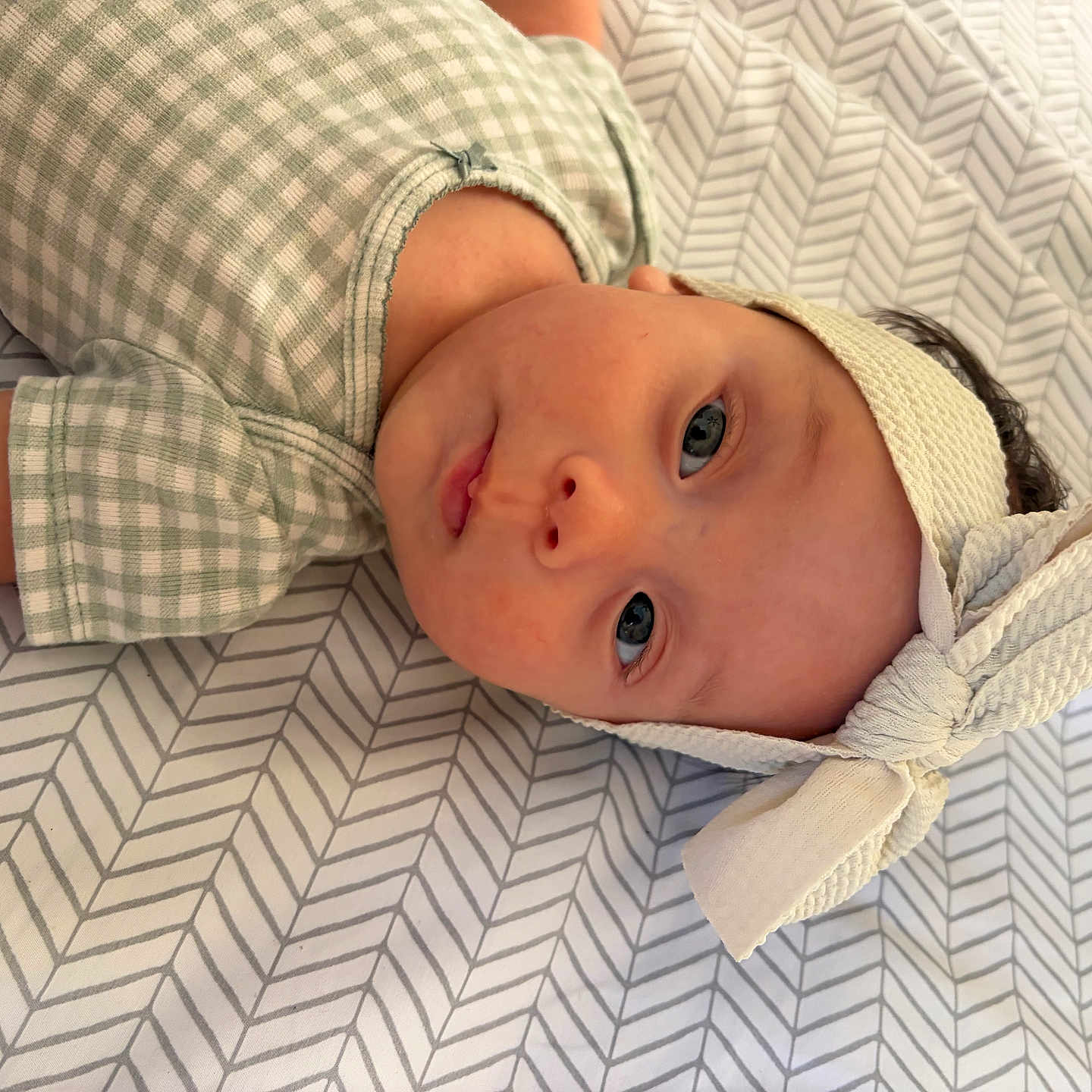 Aitana joined the competition — help win amazing prizes! baby, infant, child, portrait, lying_down, headband, bow, onesie, plaid_clothing, blanket, bedding, patterned_background, zigzag_pattern, wide_eyes, face, eyes, indoor, cozy, photography, adorable