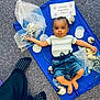 baby, child, carpet, blue_cloth, flowers, teddy_bear, decorations, striped_shirt, denim_shorts, barefoot, curious_expression, socks, polka_dot, floor, sign, indoor, playful, person, head, hands