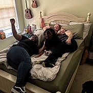 Moose is registered to the contest to win money with this photo: bed, bedroom, blanket, books, bookshelf, carpet, casual_clothing, dog, friendship, glasses, guitar, indoor, people, pillow, relaxing, rottweiler, smiling, sneakers, tattoo, window