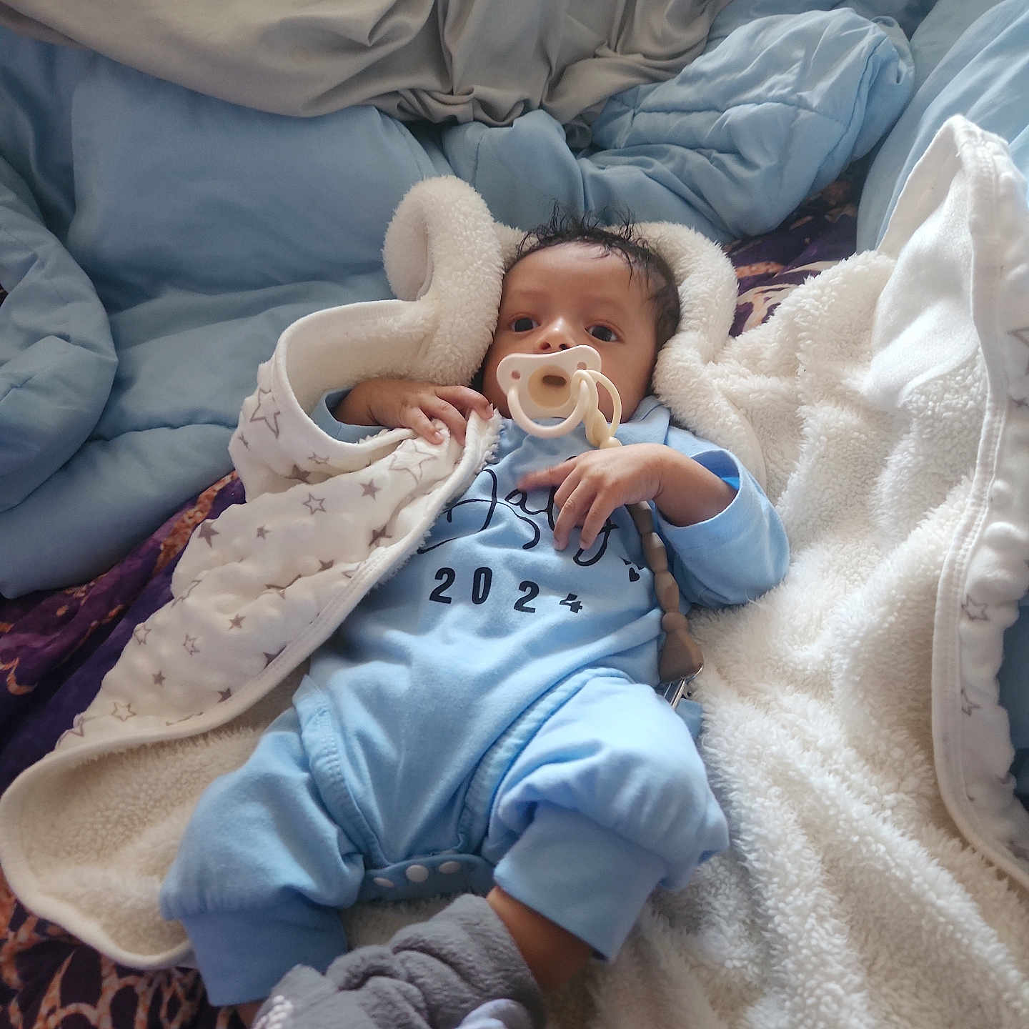Zion is registered to the contest to win money with this photo: baby, bed, blanket, bodypart, clothing, couch, crib, face, finger, furniture, glove, hand, happy, head, infantbed, newborn, person, photography, portrait, smile