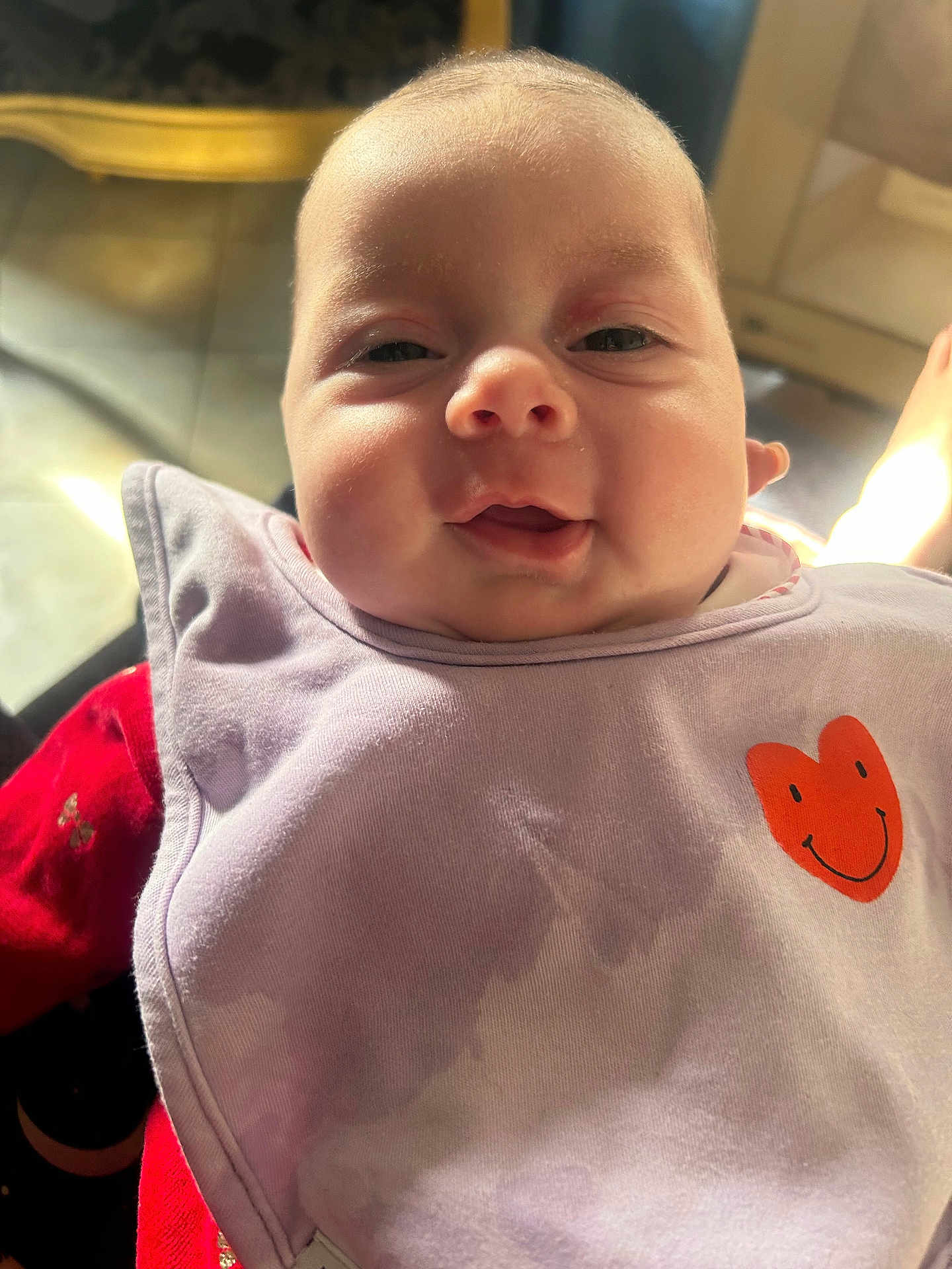 Talya a rejoint le concours — aidez-le/la à gagner de superbes lots ! baby, smiling, face, bib, orange_heart, red_clothing, indoor, natural_light, floor, foot, person, closeup, happy, child, young, infant, portrait, cute, wearing, fabric