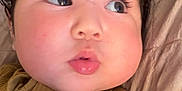 Lilith Sorrow is registered to the contest to win money with this photo: baby, close_up, face, child, curly_hair, cheeks, eyes, mouth, expression, mustard_clothing, ribbed_fabric, quilted_blanket, skin, portrait, infant, lying_down, cute, soft_lighting, indoors, young_child