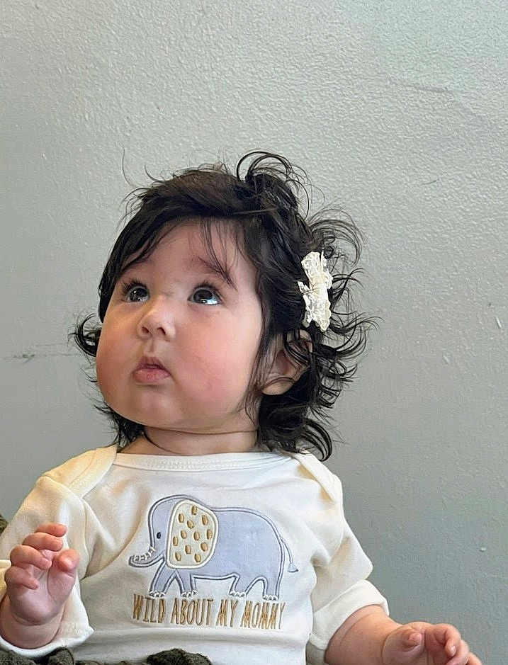 Lilith Sorrow joined the competition — help win amazing prizes! baby, child, infant, portrait, curly_hair, hair_clip, white_shirt, elephant_graphic, text_on_clothing, looking_up, cute, indoors, sitting, expression, face, skin, young, person, clothing, toddler