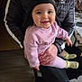 baby, child, person, smiling, cap, pink_clothing, sitting, adult, jacket, black_jacket, indoor, table, phone, floor, hand, yellow_socks, pants, happy, face, portrait
