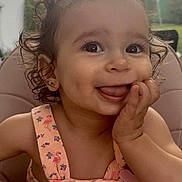 Asma participe au concours pour gagner de l'argent avec cette photo : baby, child, close_up, curly_hair, cute, daylight, earrings, flamingo_pattern, funny_face, hand_on_cheek, happy, high_chair, outdoor, person, pink_dress, portrait, seat, smiling, toddler, tongue_out