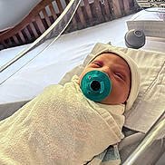 Maverick is registered to the contest to win money with this photo: baby, bassinet, bed, blanket, closeup, crib, face, hat, healthcare, hospital, indoors, infant, medical, newborn, pacifier, person, resting, sleepy, swaddled, wood