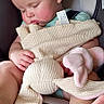 baby, infant, sleeping, car_seat, knitted_toy, stuffed_animal, bunny, blanket, clothing, portrait, indoors, travel, safety_harness, cuddling, relaxed, face, hands, feet, soft_lighting, close_up