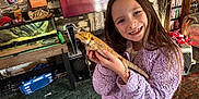 Delayni is registered to the contest to win money with this photo: child, girl, lizard, bearded_dragon, purple_jacket, smile, indoor, television, bookshelf, carpet, pet, living_room, animal, person, furniture, reptile, happy, home, long_hair, cozy