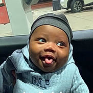 Chosen is registered to the contest to win money with this photo: baby, child, face, smile, tongue_out, hat, clothing, sweater, indoor, car_interior, window, gas_station, vehicle, person, cute, happy, portrait, infant, headwear, playful