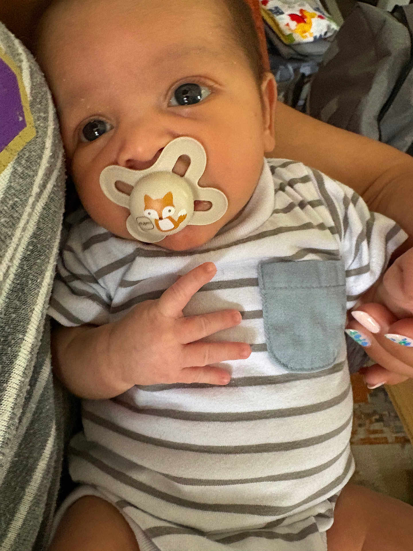 Thomas joined the competition — help win amazing prizes! baby, pacifier, striped_onesie, hand, nails, pocket, face, closeup, infant, person, holding, cute, curious, indoor, skin, eyes, fingers, clothing, adult_hand, comfort