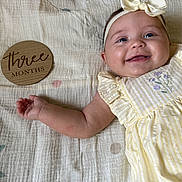 Lainey joined the competition — help win amazing prizes! baby, smiling, headband, dress, yellow, striped, plaque, wooden, blanket, patterned, child, happy, face, infant, cute, lying_down, portrait, small_hand, blue_eyes, indoor