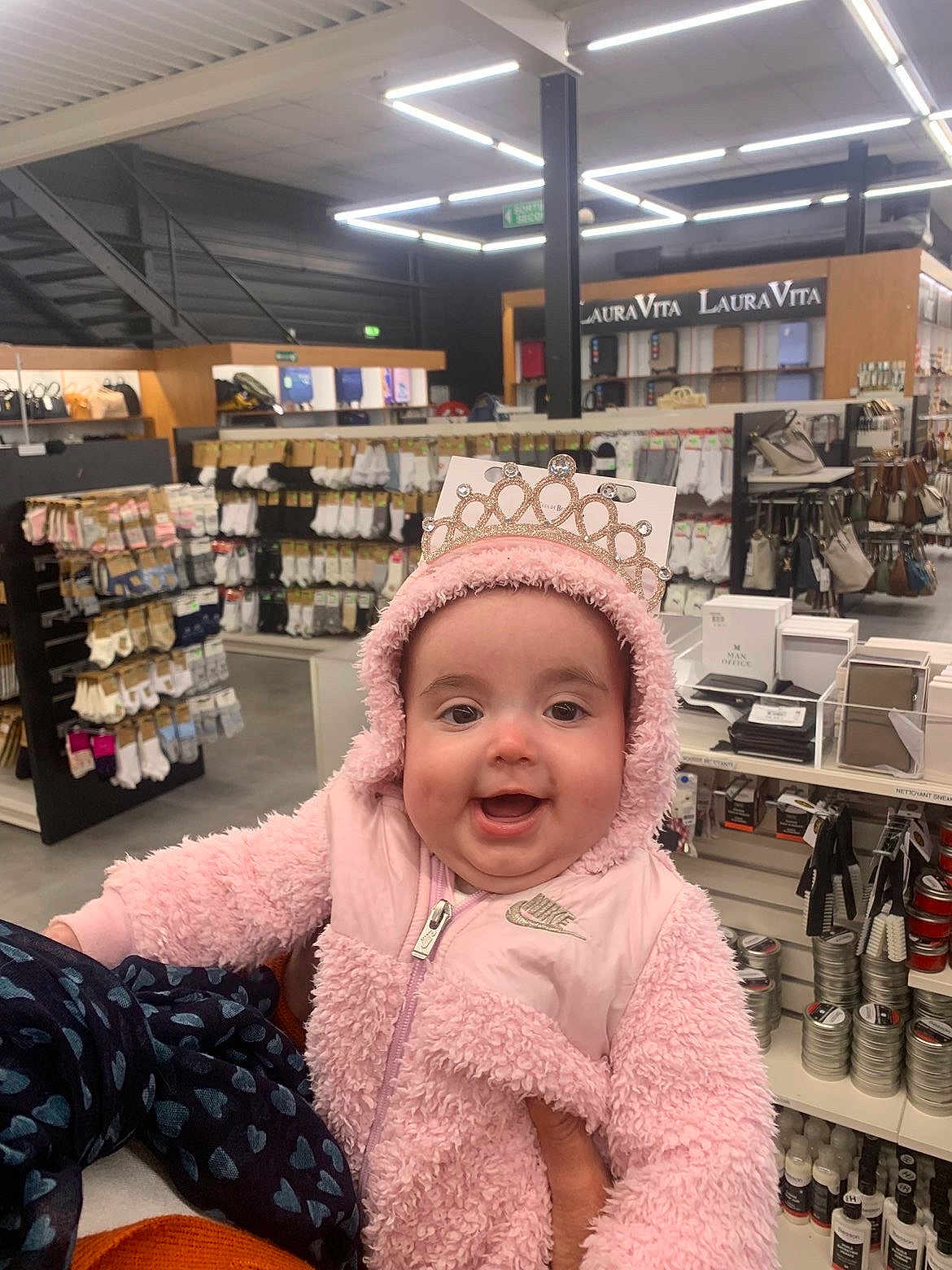 Thanaïs a rejoint le concours — aidez-le/la à gagner de superbes lots ! baby, infant, smiling_baby, pink_hood, tiara, fluffy_jacket, shopping_store, retail_shelves, sock_display, hand_holding, happy_expression, chubby_cheeks, zipper, store_lighting, accessory_display, handbags, products, aisle, portrait, cute