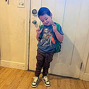 Maverick is registered to the contest to win money with this photo: child, boy, indoor, standing, backpack, tshirt, skeletal_graphic, pants, sneakers, wooden_floor, door, light_switch, playful, smiling, pose, casual, young, wall, feet, home