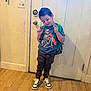 child, boy, indoor, standing, backpack, tshirt, skeletal_graphic, pants, sneakers, wooden_floor, door, light_switch, playful, smiling, pose, casual, young, wall, feet, home