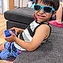 Ollie is registered to the contest to win money with this photo: child, boy, sunglasses, toy, couch, indoor, smile, tank_top, shorts, blue, black_hair, wooden_floor, furniture, relaxing, happy, casual, person, living_room, playful, home