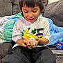 Ollie joined the competition — help win amazing prizes! child, hamster, couch, blanket, toy, clothing, person, indoor, happy, animal, pet, black_pants, short_hair, smiling, cute, cozy, pikachu, holding, furniture, playing