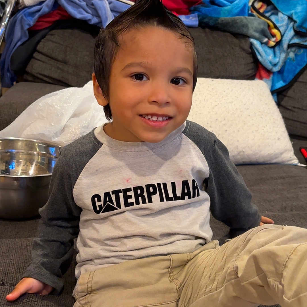 Ollie is registered to the contest to win money with this photo: blankets, boy, casual_clothing, caterpillar_shirt, child, couch, cute, happy, home, indoor, living_room, metal_bowl, mohawk, pants, playful, portrait, relaxed, seated, smile, young